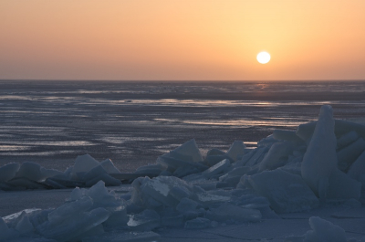 De ondergaande zon beschijnt het kruiende ijs op het IJsselmeer en zet het geheel in een zachtblauwe gloed.