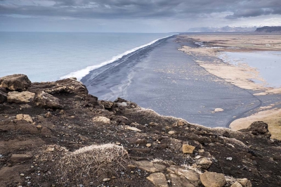 Onderwerp in het midden (strand). Voorgrond de rand van de klif. De bergen op de achtergrond.