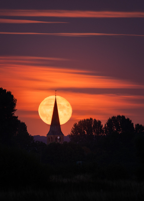 Het idee begon in gedachten met een opkomende volle maan boven landschap. Eenmaal in het veld met wat apps uitgevogeld waar 'precies' de opkomst zou zijn en besloten het kerkje als uitgangspunt te nemen. Na een 20-30 minuten heen en weer wandelen, precies de juiste lijn bepaald zodat de maan links uit de bomen ophoog zou komen.
Daarna wachten tot het gaat gebeuren en hopen dat de wolken een beetje meewerken! Het spektakel speelt zich vlak na zonsondergang af dus met wat geluk barst het van de kleuren.
