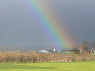 Deze regenboog kwam te voorschijn toen er een onweersbui dichterbij kwam. Op de achtergrond een boerenbedrijf in de zon